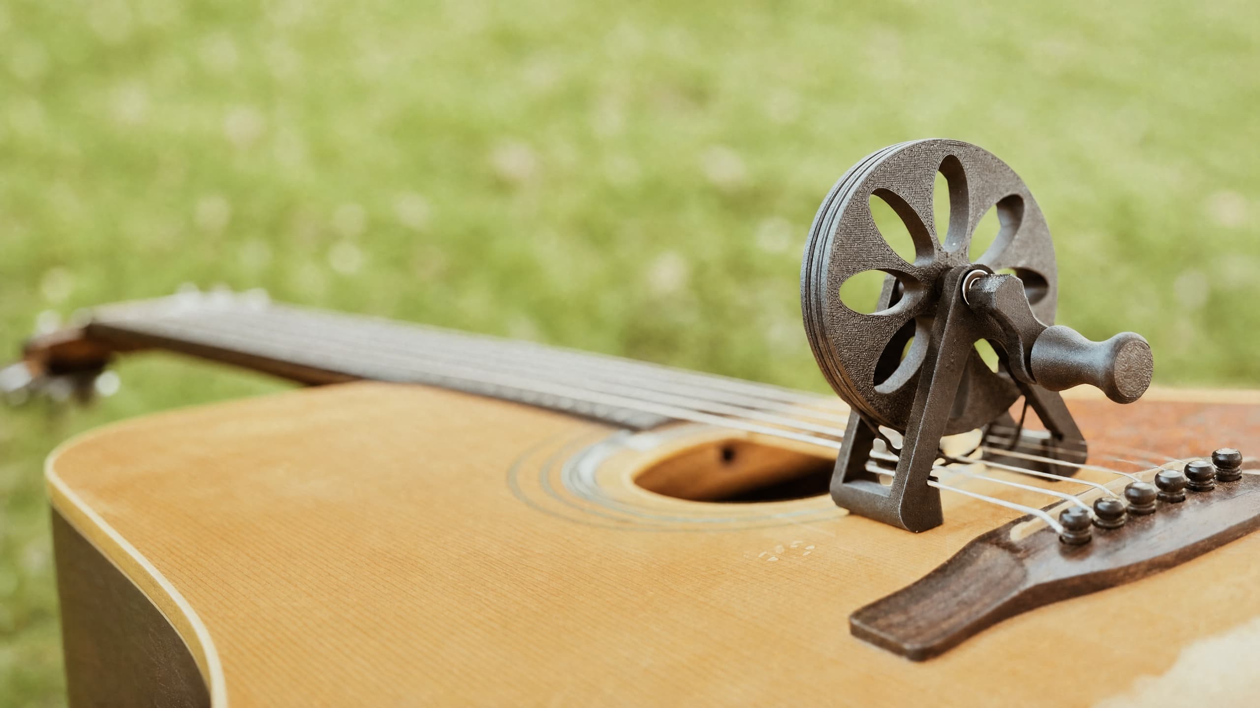 An acoustic guitar lying in a grassy field with the Cloverwheel, a black spoked wheel, mounted over the strings beside the soundhole